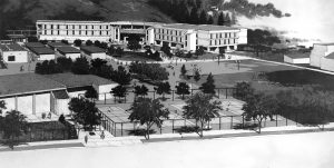 Architects Rendering of the New School 1970 The original school buildings ,though restorable, were torn down for safety reasons. A new campus was designed in contemporary “brutalist “style and built to segue with the demolition. The new classroom buildings were nestled against the hills, with the grounds and smaller buildings forming a garden court in front. On the left is the new small gym. The corner of the auditorium is at right.